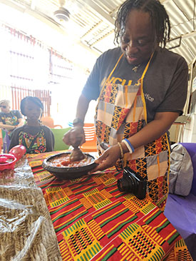 A child watches as a person in a brightly color apron prepares a traditional Ghanaian dish