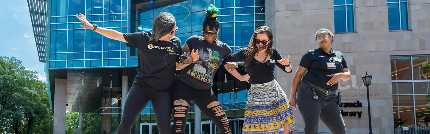 Four students dance together in front of VCU's library.