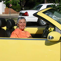 A woman sits in a yellow Volkswagen Beetle convertible