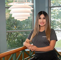 A student wearing a gray VCU shirt stands with an arm against a stair railing as a lantern-style light fixture hangs to the left.