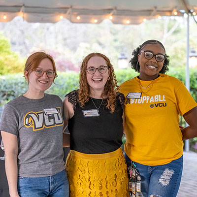 Two students in gray and gold VCU t-shirts, respectively, stand on either side of the school's senior development specialist, wearing a black top and gold skirt.